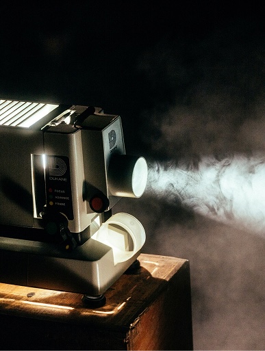Projecteur de film Dukane projetant de la fumée, évoquant une ambiance de consultation en expérience client.