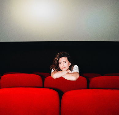 Jeune personne assise dans un cinéma avec les bras croisés sur le dossier.