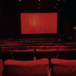 Salle de cinéma vide avec sièges rouges et écran de rideau rouge, pour le marketing expérientiel en entreprises.