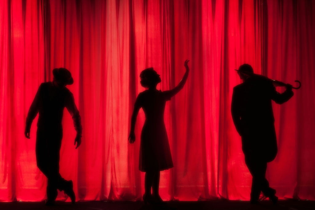 Silhouettes d'artistes de théâtre sur scène rouge.
